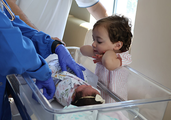 Cecilia's son Sebastian look at his new baby sister as the doctor exams her in the bassinet