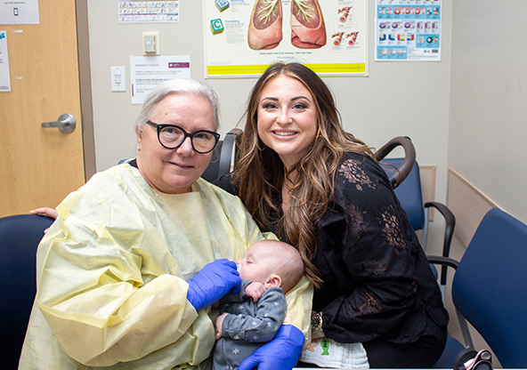 Dr. Giles holds baby Warren and poses with Kendall Nolte at Warren's follow-up visit