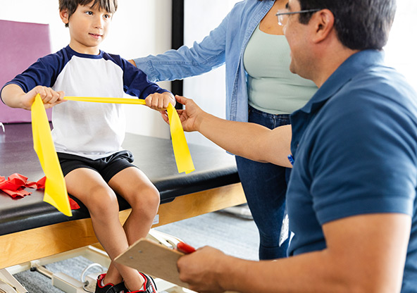 A boy uses a resistance band at physical therapy