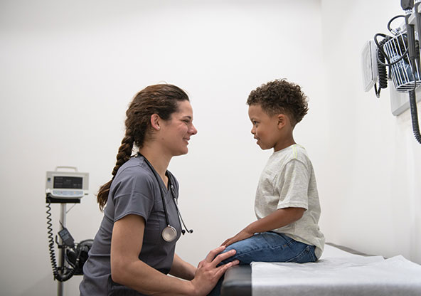 A nurse at an urgent care smiling at a young boy who is sitting on the exam table and smiling at her